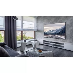 Un salon moderne présente l'élégant téléviseur SAMSUNG TQ77S95D avec une superbe scène de montagne, complétée par de grandes fenêtres qui laissent entrer la lumière naturelle et une table basse minimaliste améliorant l'ambiance tranquille.