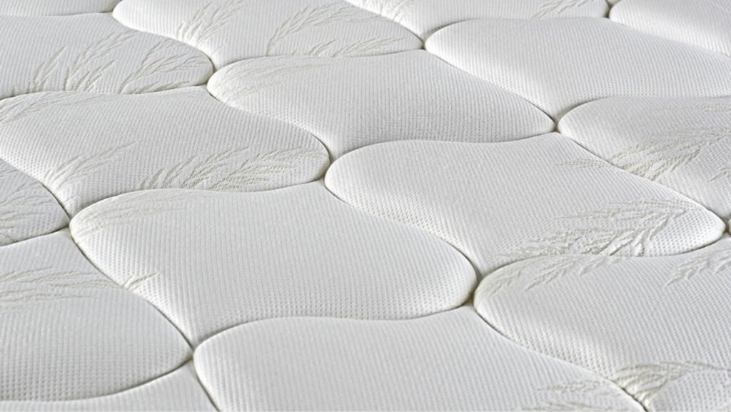 Gros plan sur la surface du matelas EPEDA EMBRUN, qui présente un matelassage blanc avec un motif ondulé et de subtils dessins de feuilles.