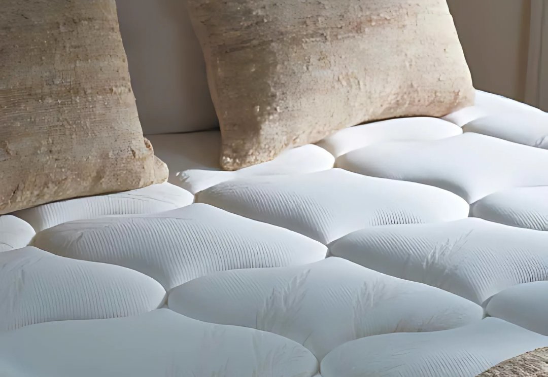 Gros plan sur le matelas EPEDA EMBRUN en blanc avec une finition matelassée, surmonté de deux oreillers beiges placés contre la tête de lit.