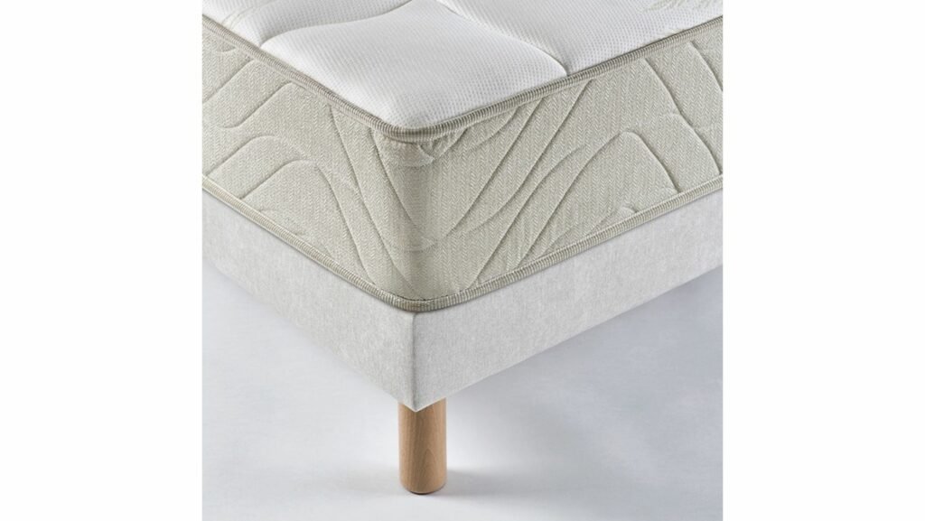 Gros plan d'un coin matelas EPEDA EMBRUN avec une housse texturée blanche sur un pied de cadre de lit en bois.