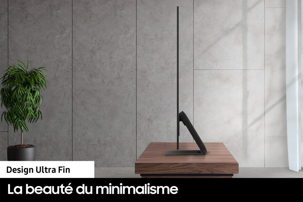 Vue latérale du moniteur SAMSUNG TQ55S95C posé sur un bureau en bois avec une plante à proximité, mettant en valeur son design minimaliste. Texte : « La beauté du minimalisme.