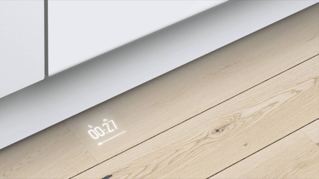 Un affichage d'horloge numérique projeté sur un plancher en bois clair à côté d'armoires de cuisine blanches et d'un élégant lave-vaisselle intégré BOSCH SMV6ECX00E.