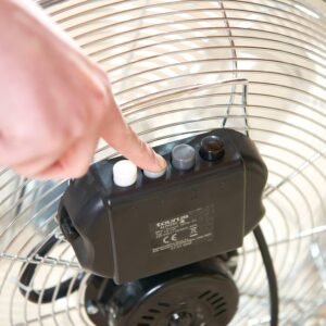 Gros plan d'une main appuyant sur un bouton du panneau de commande noir élégant du ventilateur en métal TAURUS SIROCCO 14 avec un couvercle en grille.
