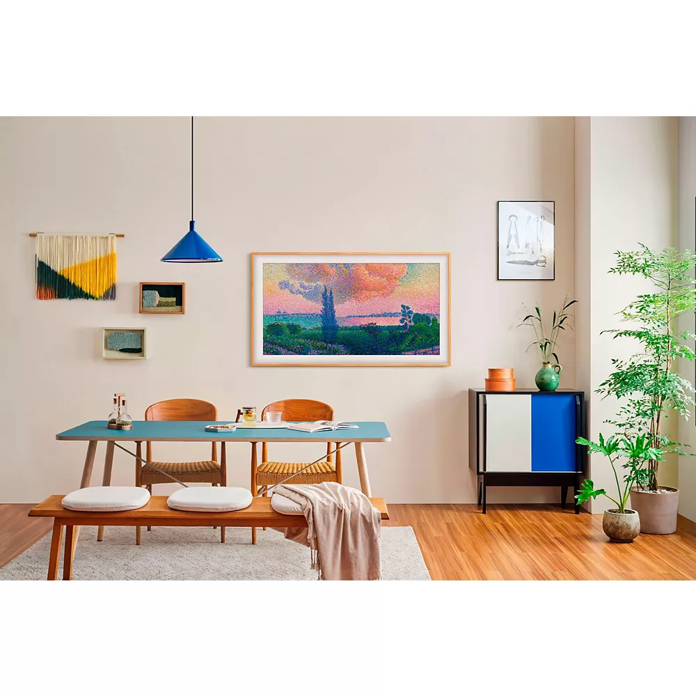Salle à manger moderne avec une table en bois, des accents bleus, des œuvres d'art murales, des plantes vertes et un parquet, avec le téléviseur intelligent SAMSUNG TQ43LS03B se fondant parfaitement dans le décor pour une fusion élégante de technologie et de design.