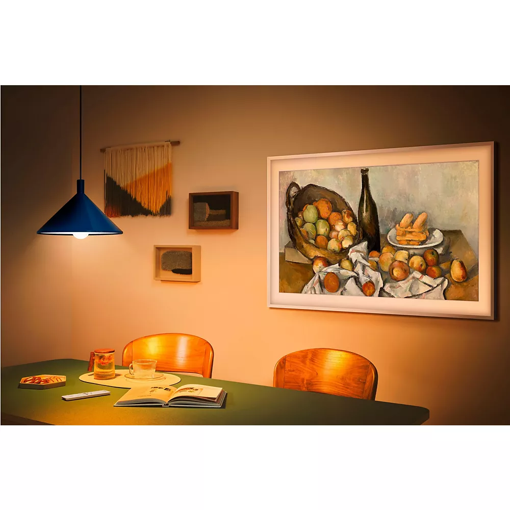 Une salle à manger confortable avec une table, des chaises, des œuvres d'art murales et une lumière suspendue chaleureuse, mettant en vedette le SAMSUNG TQ43LS03B se fondant parfaitement dans une œuvre d'art numérique élégante au-dessus de la table dressée.