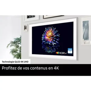 Un téléviseur SAMSUNG TQ43LS03B affiche une fleur vibrante sur son écran, montée sur un mur blanc au milieu d'œuvres d'art encadrées.