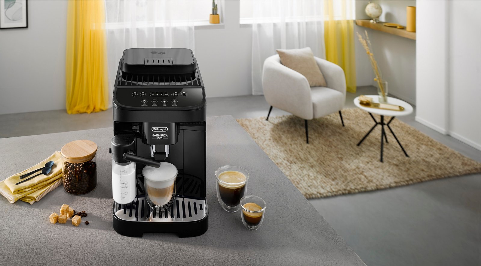 Une machine à café moderne noire DELONGHI ECAM293.52B MAGNIFICA est posée sur le comptoir de la cuisine avec deux tasses de café riche et un salon confortable en arrière-plan.