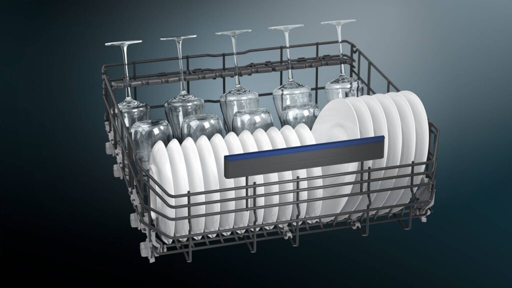 Un panier de lave-vaisselle SIEMENS SN65EX10CE rempli de verres à vin et d'assiettes propres, vu de face sur un fond sombre.