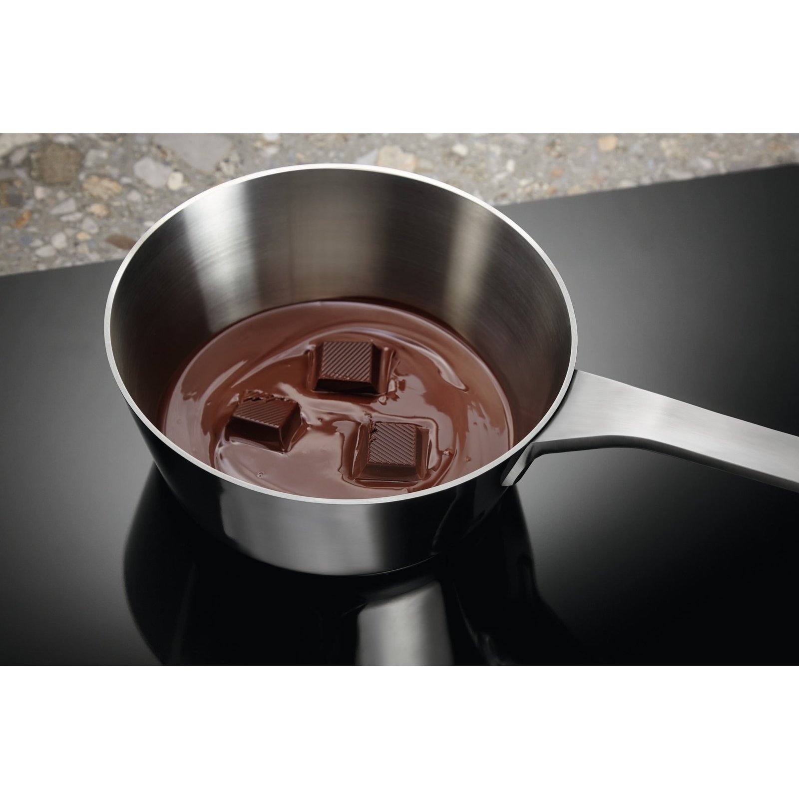 Trois morceaux de chocolat fondent dans une casserole en acier inoxydable sur une cuisinière noire ELECTROLUX EIV63343.