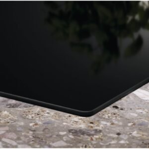 Gros plan du coin d'une surface en verre noir sur un comptoir en pierre mouchetée avec un reflet vert flou, mettant en valeur le design moderne de l'ELECTROLUX IDE6342KC.