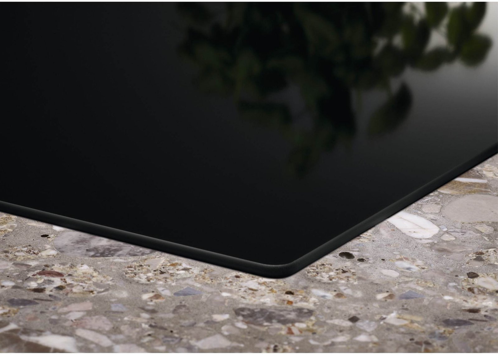 Gros plan du coin d'une surface en verre noir sur un comptoir en pierre mouchetée avec un reflet vert flou, mettant en valeur le design moderne de l'ELECTROLUX IDE6342KC.