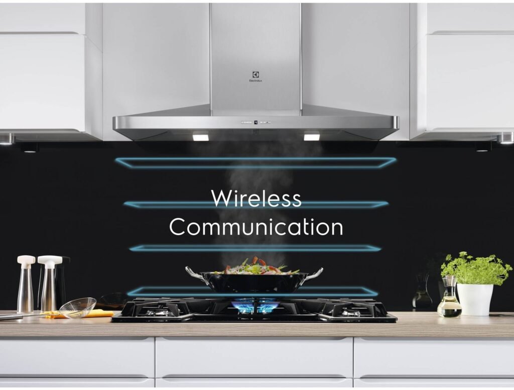 Dans une cuisine moderne, une table de cuisson grésille de légumes dans un wok, tandis que les mots « Communication sans fil » s'illuminent sur un dosseret noir rétroéclairé, mettant en vedette l'élégant ELECTROLUX IDE6342KC pour une expérience de cuisson innovante.