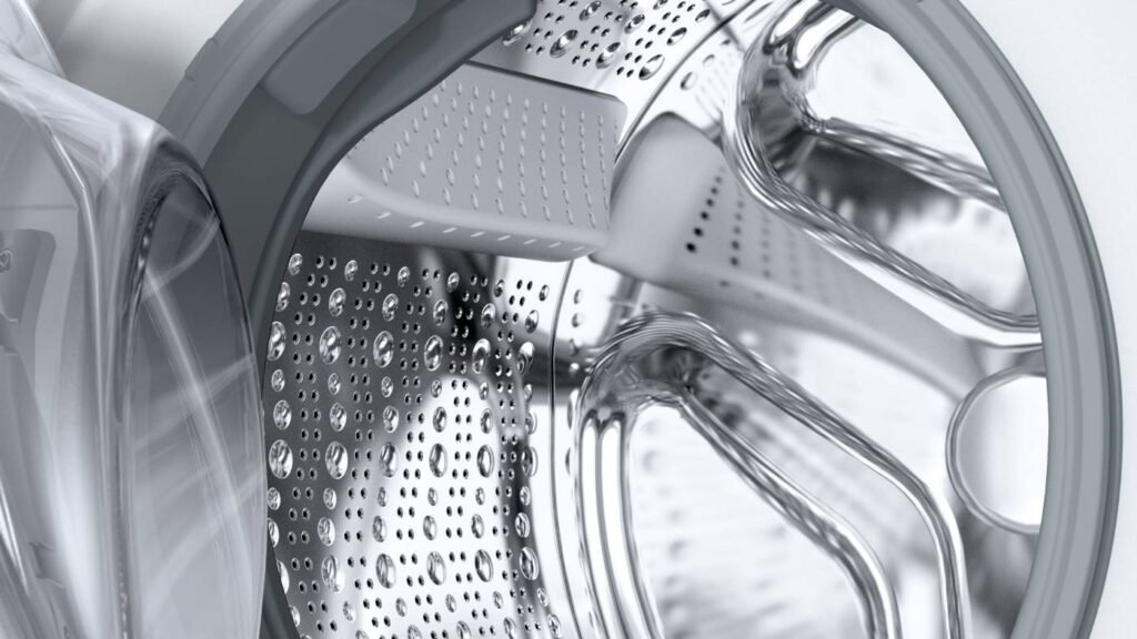 Gros plan de l'intérieur du tambour d'une machine à laver SIEMENS WG44G2F2FR, présentant des gouttes d'eau scintillant sur la surface métallique.