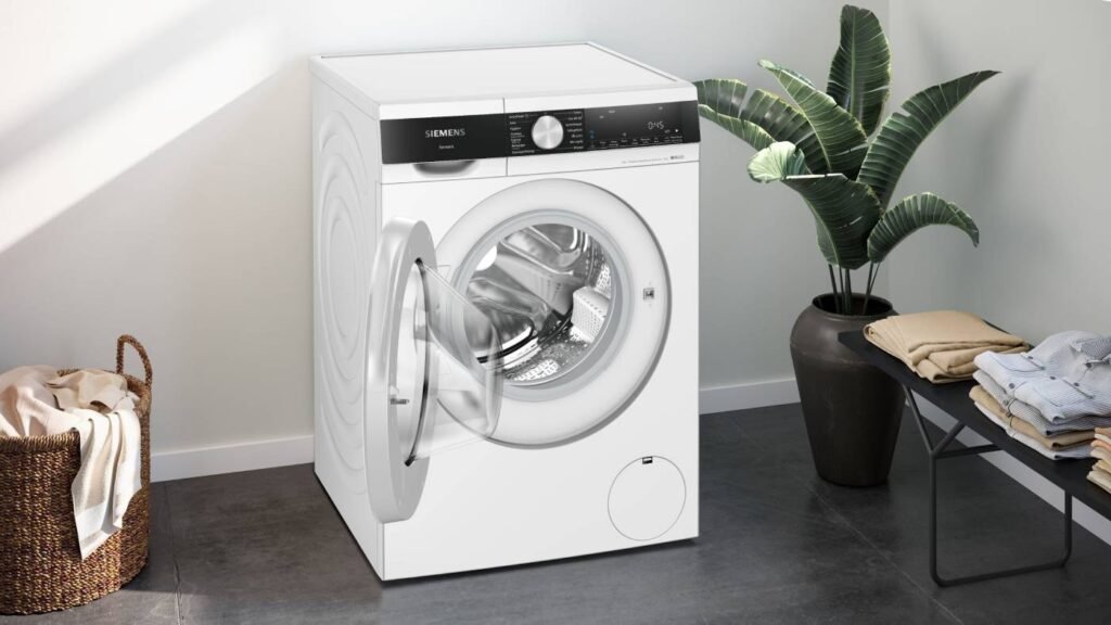 La buanderie moderne est élégamment décorée d'une élégante machine à laver à chargement frontal SIEMENS WG44G2F2FR blanche, complétée par une plante en pot et des vêtements soigneusement pliés à proximité.