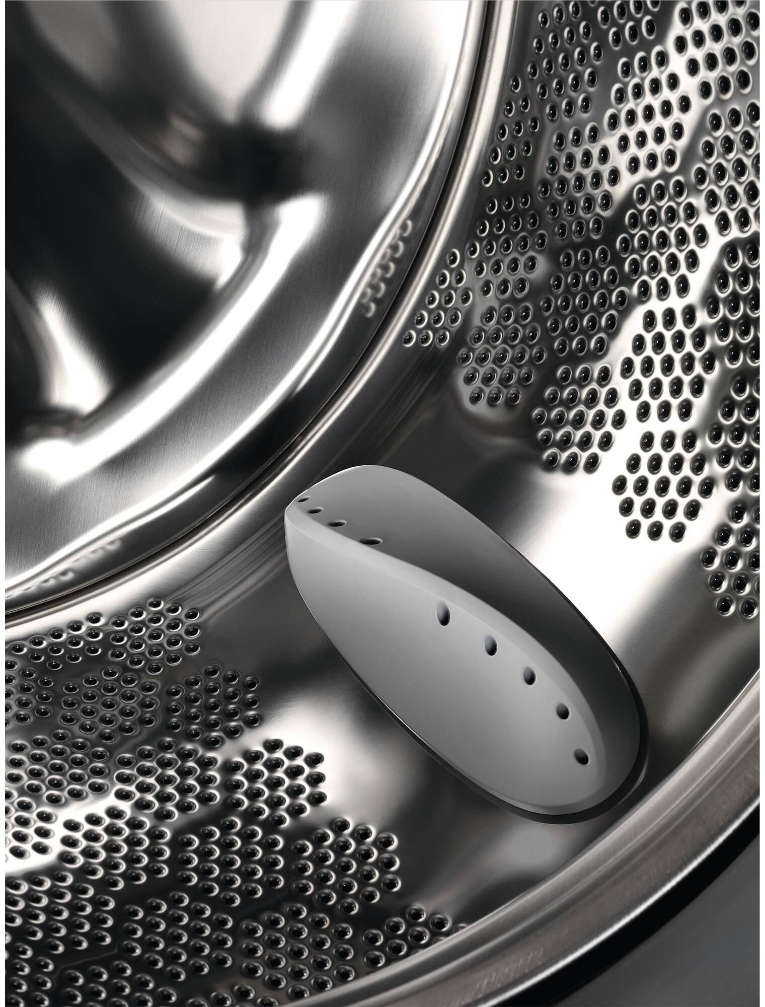 Gros plan d'un tambour de machine à laver en acier inoxydable brillant avec des trous perforés, mettant en valeur le design élégant du modèle ELECTROLUX EW6F5814BA.