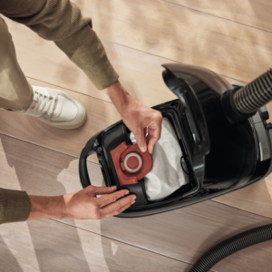 Quelqu'un remplace le sac d'un élégant aspirateur Miele GUARD M1 FLEX sur un plancher en bois poli.