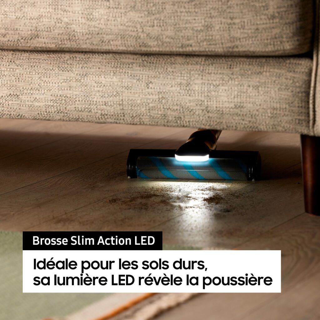 Gros plan de l'aspirateur SAMSUNG VS20C85G4TB équipé d'un éclairage LED, éliminant efficacement la poussière sous un canapé sur un sol dur.