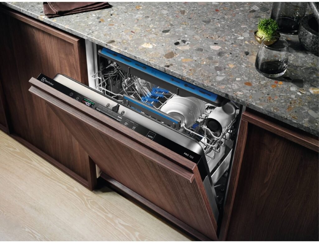 Meuble ouvert en bois comportant un lave-vaisselle ELECTROLUX EES48320L, rempli de vaisselle, sous un comptoir moucheté.