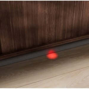 Un point laser rouge danse sur le plancher en bois devant un meuble, projetant des reflets subtils près des lignes épurées d'un lave-vaisselle ELECTROLUX EES48320L.