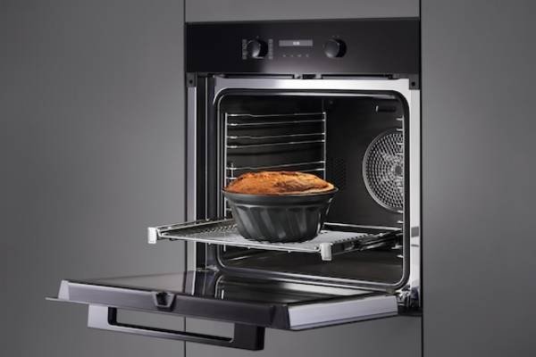 Un four MIELE H2766BP NOIR ouvert révèle un gâteau dans un moule rond sur la grille coulissante, mettant en valeur la perfection de la cuisson.