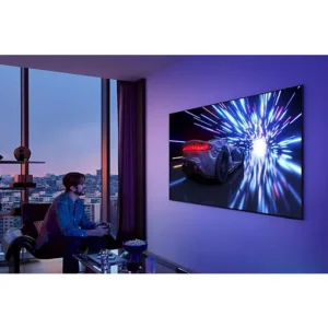 Un homme joue à un jeu vidéo de course sur le téléviseur mural SAMSUNG TQ65S95F dans un salon moderne.