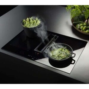 La cuisinière élégante FALMEC QUANTUM3421 EASY avec évent intégré cuit sans effort des casseroles de légumes à la vapeur, tandis que des légumes-feuilles vibrants et des citrons verts reposent à proximité dans un bol.