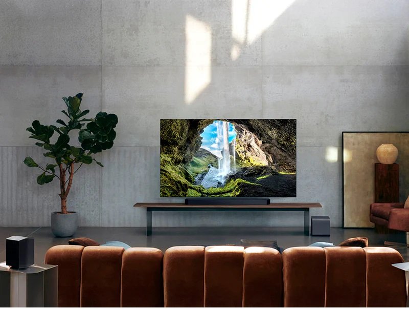 Salon moderne avec une grande télévision montrant la nature, un canapé marron, une plante en pot et une élégante barre de son SAMSUNG HW-Q995D (Copie) pour un son immersif.