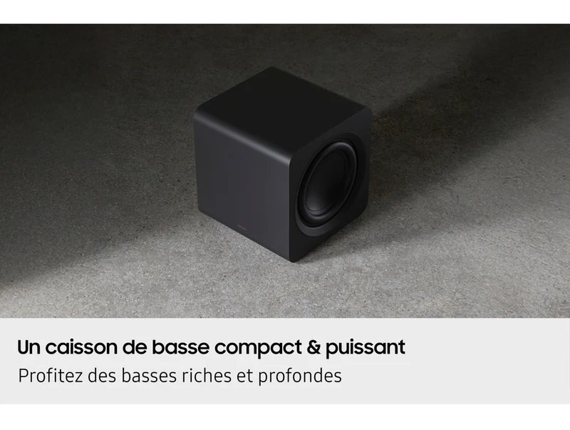 Un caisson de basses compact noir SAMSUNG HW-Q995D (Copie) repose sur une surface grise, avec un texte français soulignant ses basses profondes et puissantes.
