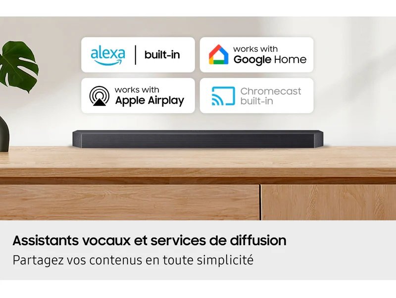 Une barre de son SAMSUNG HW-Q995D (Copie) repose sur une surface en bois, avec les logos Alexa, Google Home, Apple AirPlay et Chromecast affichés au-dessus.