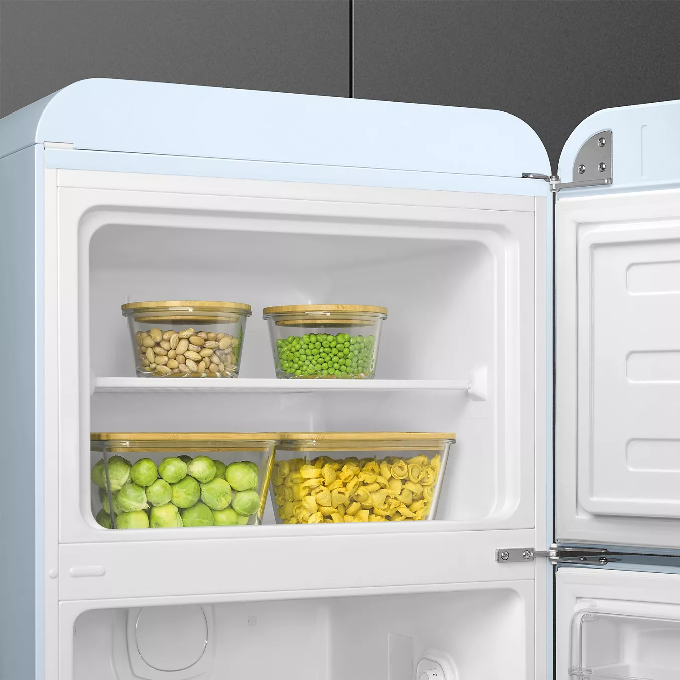 En ouvrant le réfrigérateur-congélateur SMEG FAB30RPB5, vous trouverez quatre bacs de légumes surgelés, tels que des petits pois et des choux de Bruxelles, bien rangés sur deux étagères.