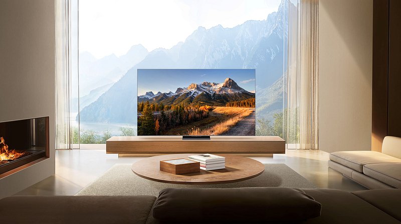 Salon moderne doté d'un grand téléviseur TCL 75C8K affichant un paysage de montagne, avec une cheminée et une vue imprenable sur les montagnes visibles à travers de hautes fenêtres.