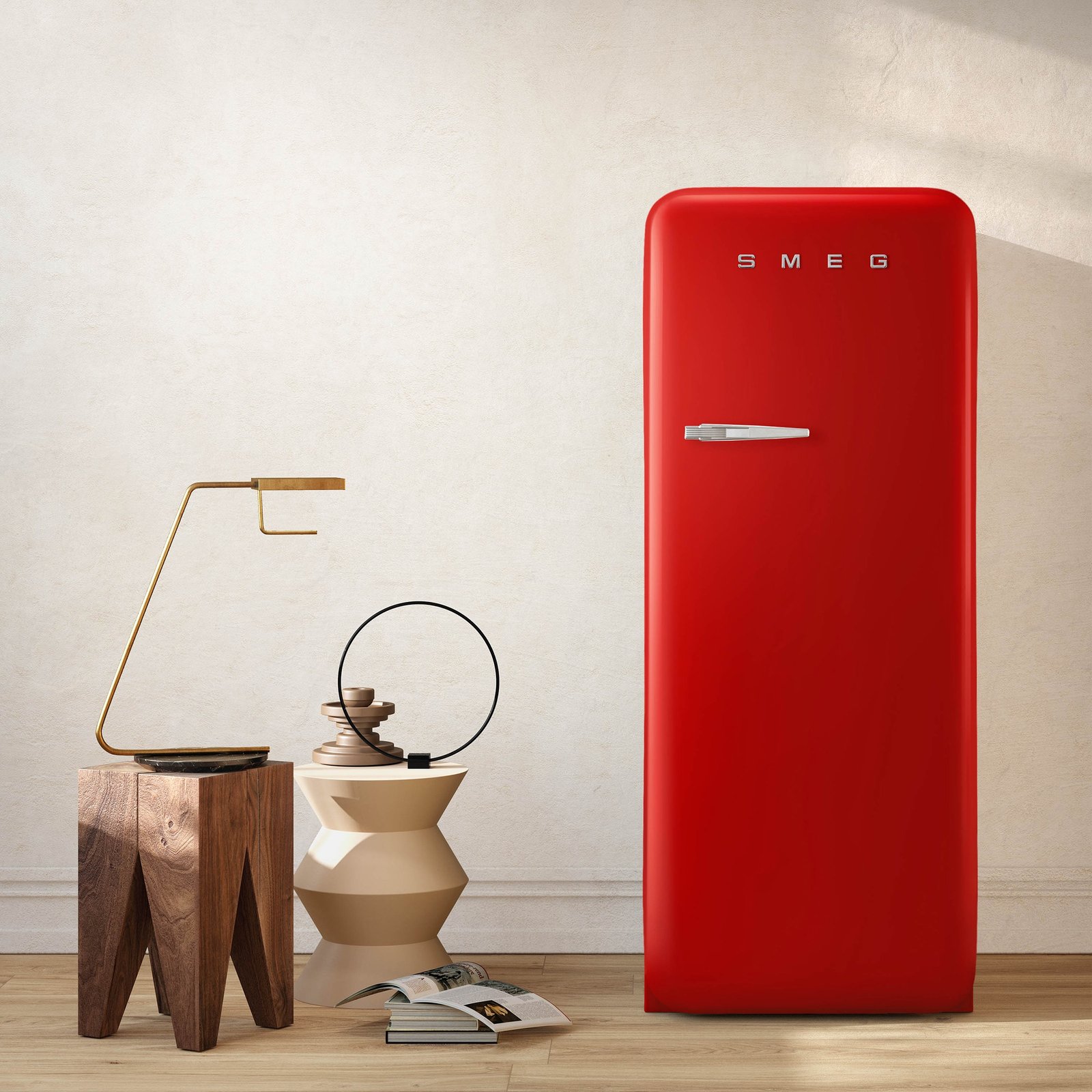 Un grand réfrigérateur rouge SMEG FAB28RRD6 se trouve à côté de tables modernes en bois et en céramique avec un décor minimaliste et un livre ouvert.