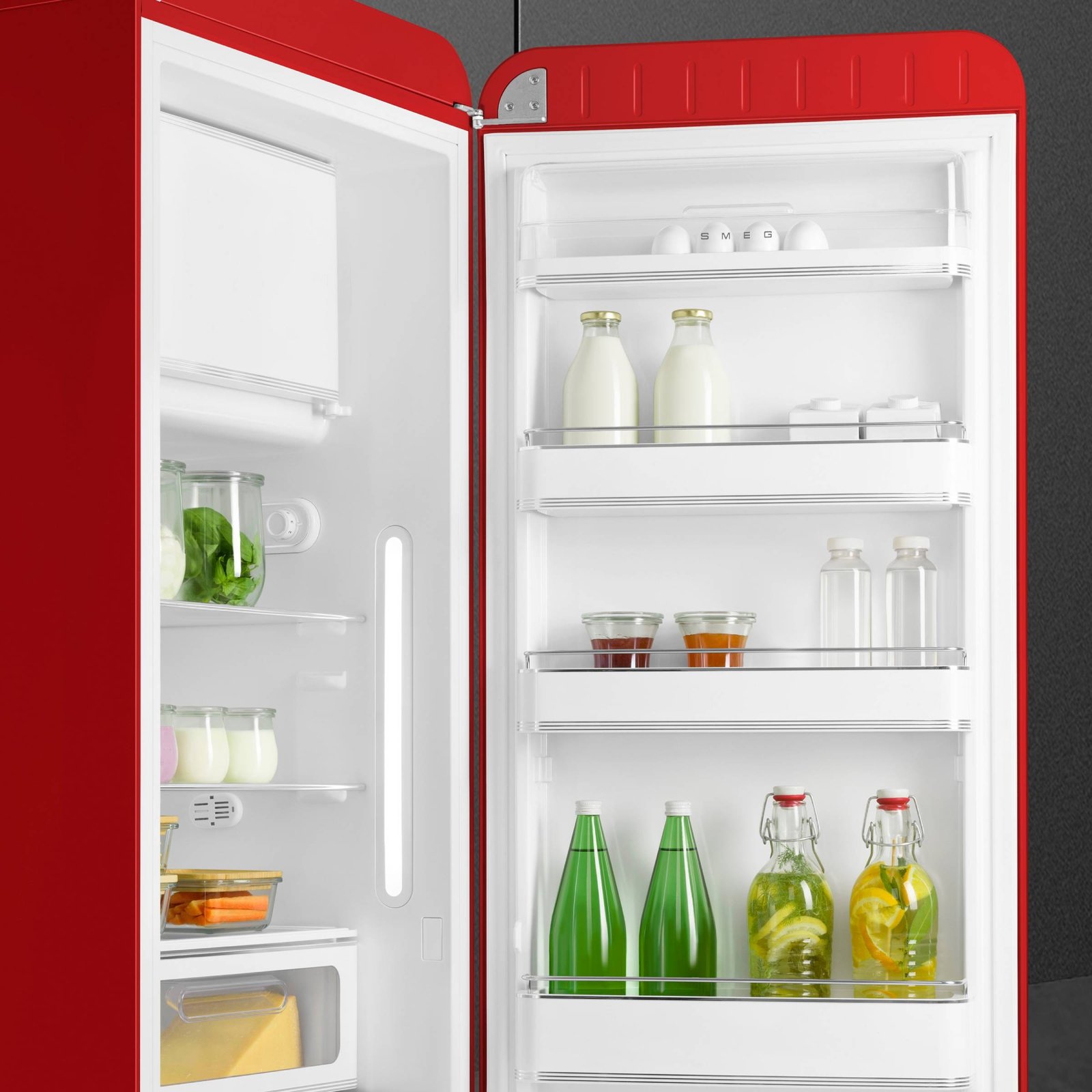 Réfrigérateur ouvert SMEG FAB28RRD6 rouge, avec des boissons en bouteille, des bocaux et des produits frais soigneusement disposés sur des étagères et une porte, soulignant son style rétro classique.