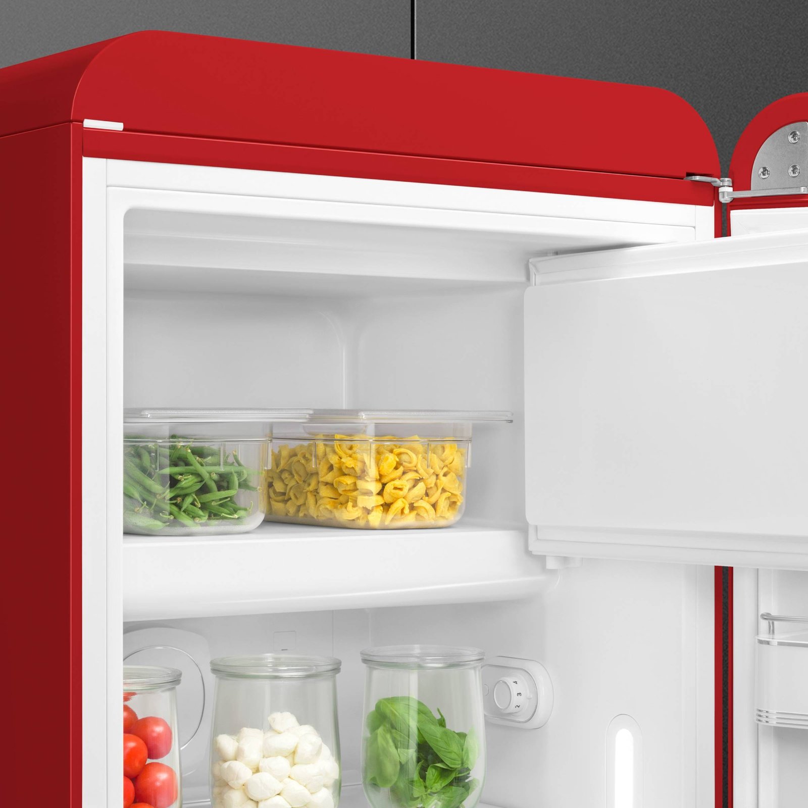 Le réfrigérateur rouge SMEG FAB28RRD6 est ouvert, montrant des légumes, des pâtes et du fromage stockés dans des récipients en verre et en plastique sur ses étagères.