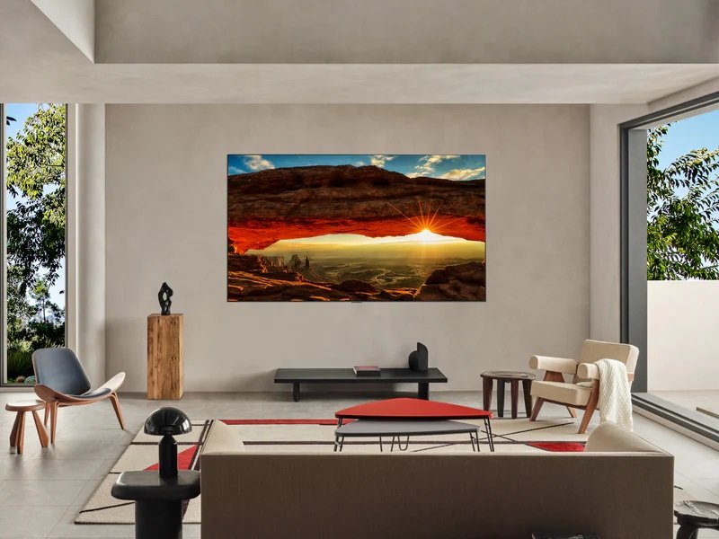 Un salon moderne et élégant met en valeur un mobilier minimaliste, une grande fenêtre et le téléviseur LG OLED77G5 2025 Gallery Design, parfaitement intégré, tel un chef-d'œuvre. Une photo de paysage sublime ce mélange parfait d'art et de technologie innovante.