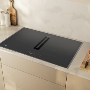 Une cuisine moderne met en valeur la table de cuisson à induction NEFF V57THQ4L0, avec des planches à découper en bois, un évier élégant et une élégante présentation de produits frais sur le comptoir.