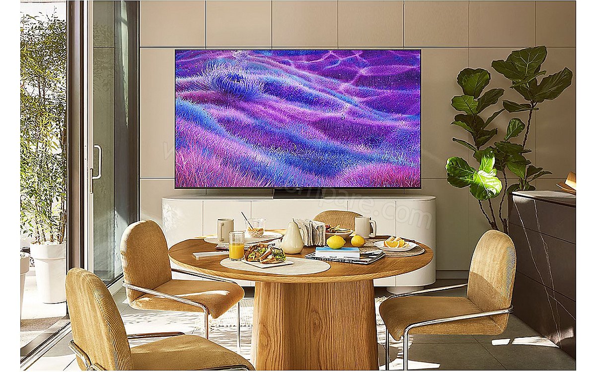 Une salle à manger moderne comprenant une table ronde, quatre chaises et un téléviseur mural SAMSUNG TQ100QN80F affichant un paysage violet.