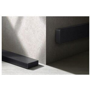 Deux barres de son SAMSUNG HW-QS760F, finies en noir, sont placées le long de la base d'angle et projettent des ombres sur une surface texturée grise.