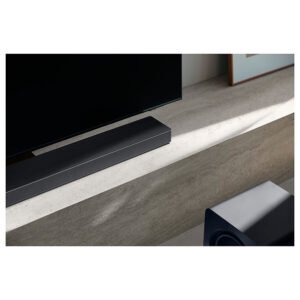 Une barre de son et un caisson de basses SAMSUNG HW-QS760F sont posés sur un meuble TV en béton élégant et léger sous un téléviseur à écran plat.