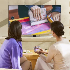 Deux personnes se détendent sur un canapé moderne, regardant une démonstration de sérigraphie sur un élégant téléviseur SAMSUNG TQ65QN90F dans leur salon.