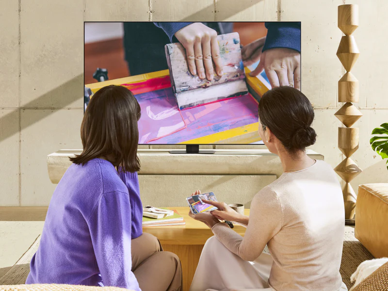 Deux personnes se détendent sur un canapé moderne, regardant une démonstration de sérigraphie sur un élégant téléviseur SAMSUNG TQ65QN90F dans leur salon.