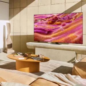 Salon moderne avec un téléviseur QLED SAMSUNG TQ65QN90F de 65 pouces affichant des œuvres d'art abstraites colorées, des canapés beiges et une table basse en bois.