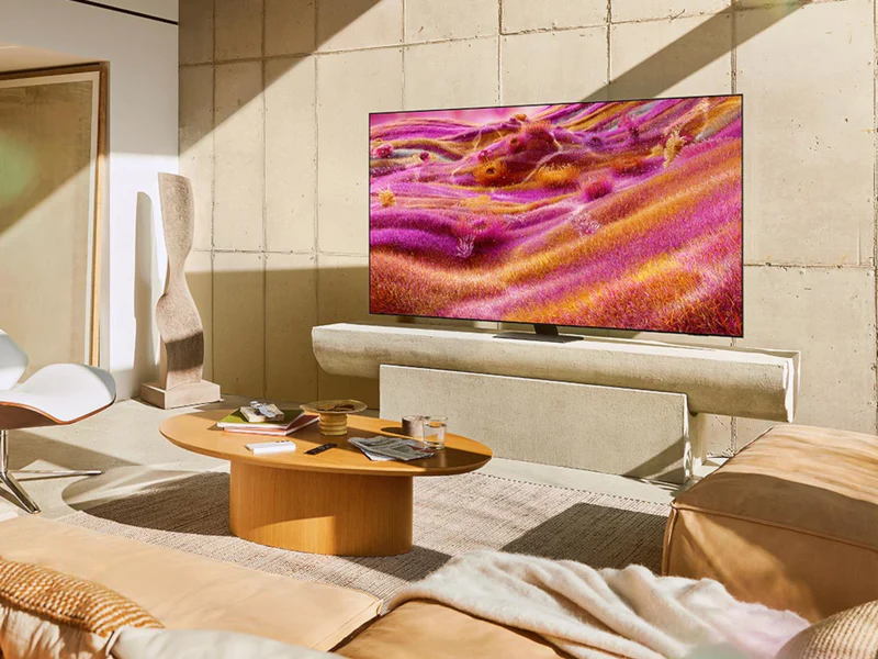 Salon moderne avec un téléviseur QLED SAMSUNG TQ65QN90F de 65 pouces affichant des œuvres d'art abstraites colorées, des canapés beiges et une table basse en bois.