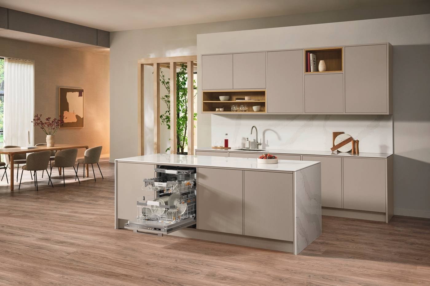 Cuisine moderne avec armoires beiges, lave-vaisselle ouvert MIELE G 7180 SCVI AUTODOS, îlot et salle à manger en arrière-plan.