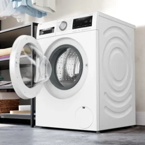 Le lave-linge BOSCH WGG254FAFR, porte ouverte, est présenté dans une buanderie moderne à côté d'étagères empilées avec des serviettes soigneusement pliées.