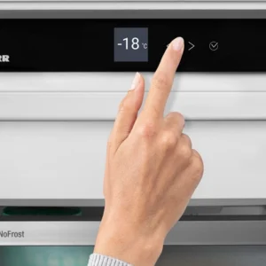 Une main ajuste le contrôle digital de la température du congélateur LIEBHERR FND7026-22, qui affiche -18°C.