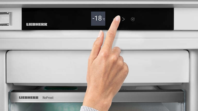 Une main ajuste le contrôle digital de la température du congélateur LIEBHERR FND7026-22, qui affiche -18°C.