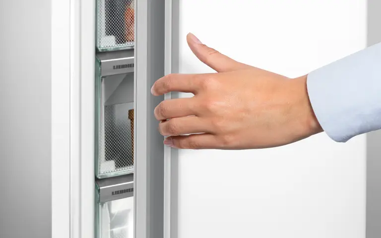 Une main ouvre la porte du réfrigérateur LIEBHERR FND7026-22, révélant ses spacieuses étagères blanches à l'intérieur.