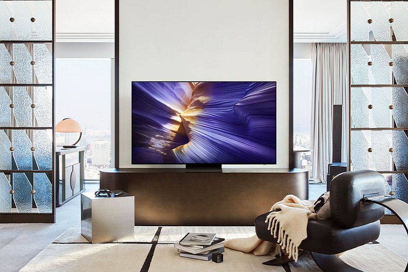 Salon moderne avec un téléviseur SAMSUNG TQ55S90F, un fauteuil noir et une vue imprenable sur la ville grâce à de grandes fenêtres.