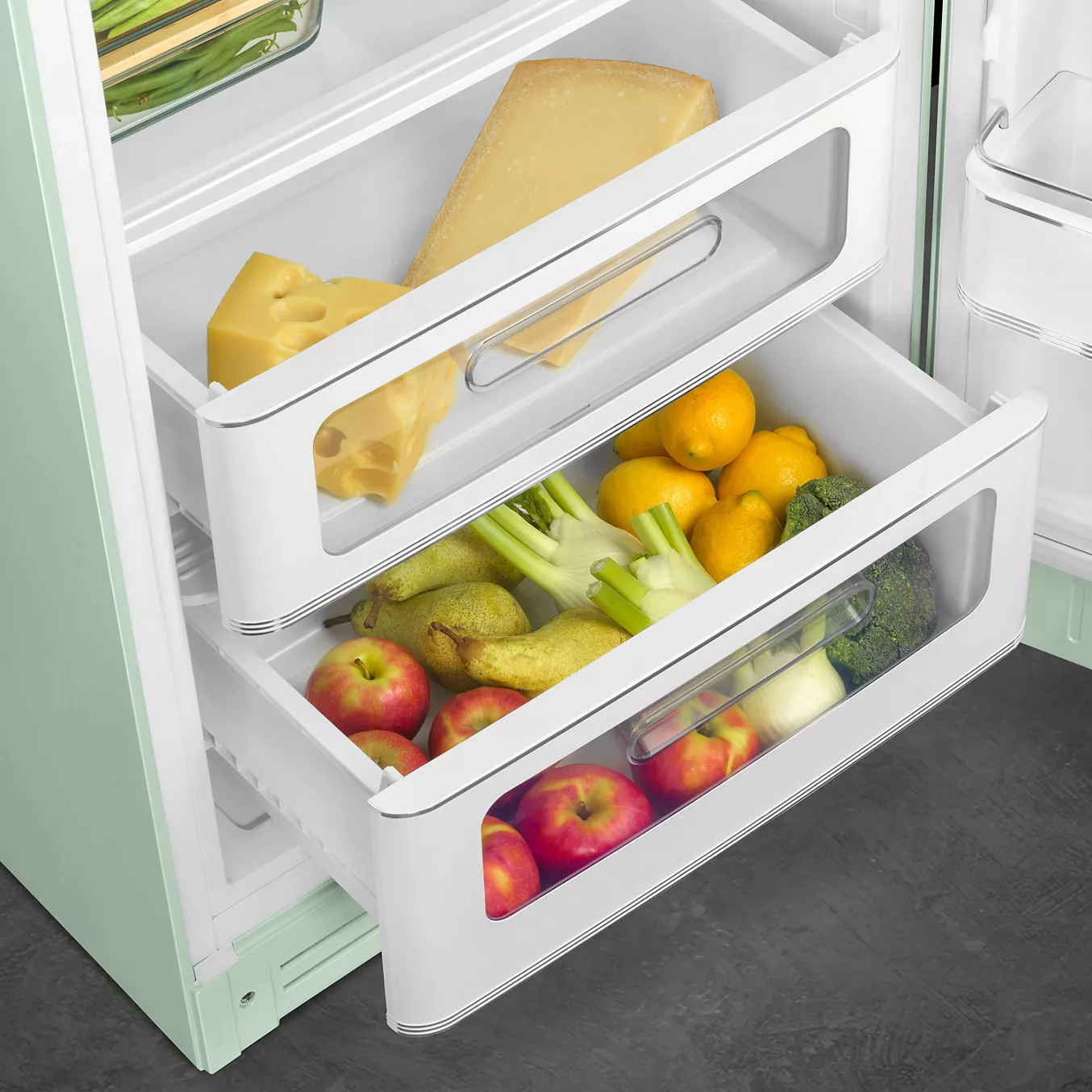 Ouvrez les tiroirs du réfrigérateur rétro SMEG FAB28RPG6 pour y trouver des pommes, des oranges, des poires, du fromage, du céleri, du brocoli et du citron.